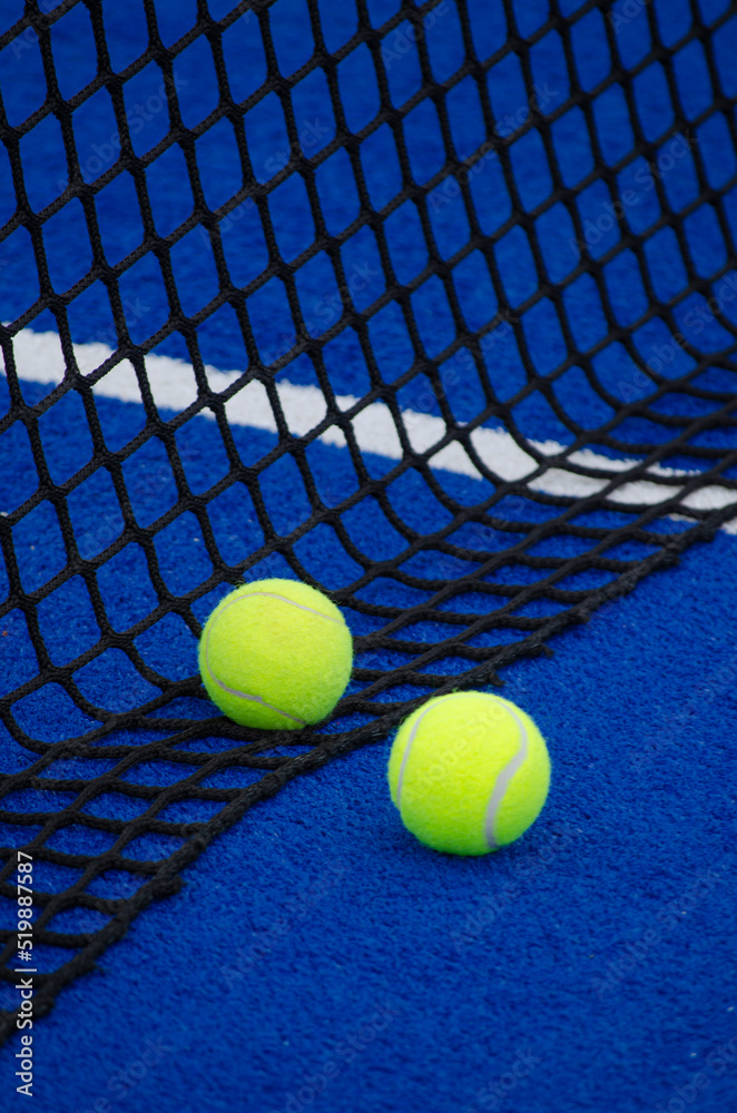 Blue paddle tennis court, two balls nearby the net