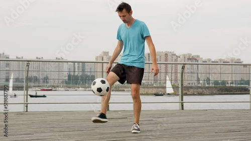 Young freestyler juggles ball doing air move tricks by river photo
