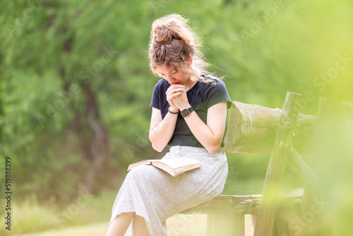 Young woman sitting on a bench praying with Bible in lap