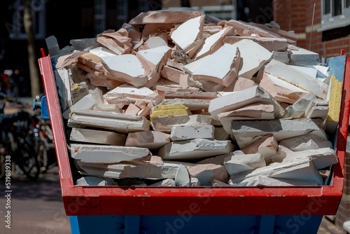 Home renovation concept,  Selective focus of waste rubble or brickbat in loaded dumpster, A construction site along street in city center, Renovated or maintenance new apartment. photo