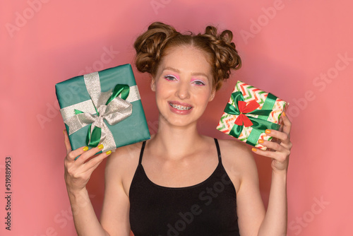 Beautiful cheerful pleased woman with red hair and big lips rejoices and feels happy holding gifts in hands on isolated background