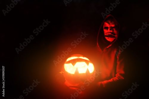 Terrible masked man Illuminated with red light from Halloween pumpkin lamp stands near the house at night. Halloween concept