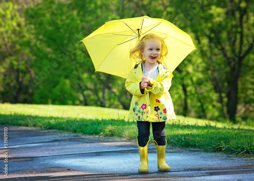 Blond toddler girl in yellow raincoat with umbrella.