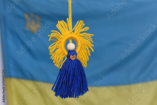 Handmade motanka doll knitted of blue and yellow threads on the background of the Ukrainian flag. Traditional amulet. photo