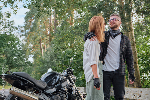 Middle age couple hugging and having fun on a motorcycle, traveling together on a forest road