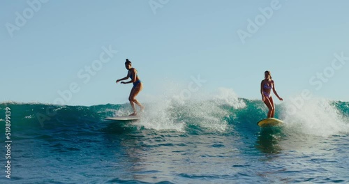 Beautiful stylish girls riding wave at sunset in Hawaii, summer lifestyle longboarding, best friends surfing together, summer lifestyle