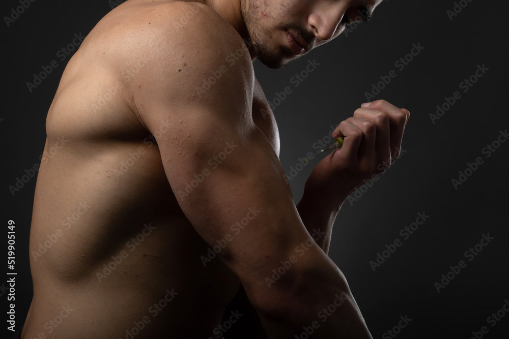 Muscular man with a syringe in his hand. User of anabolic steroids for strength training.