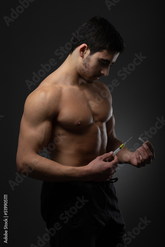 Muscular man with a syringe in his hand. User of anabolic steroids for strength training.