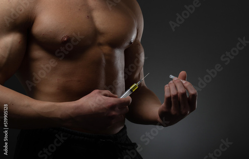 Muscular man with a syringe in his hand. User of anabolic steroids for strength training.