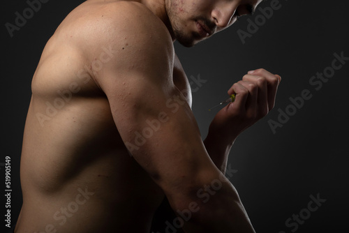 Muscular man with a syringe in his hand. User of anabolic steroids for strength training.