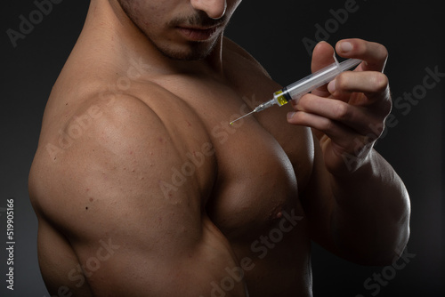 Muscular man with a syringe in his hand. User of anabolic steroids for strength training.