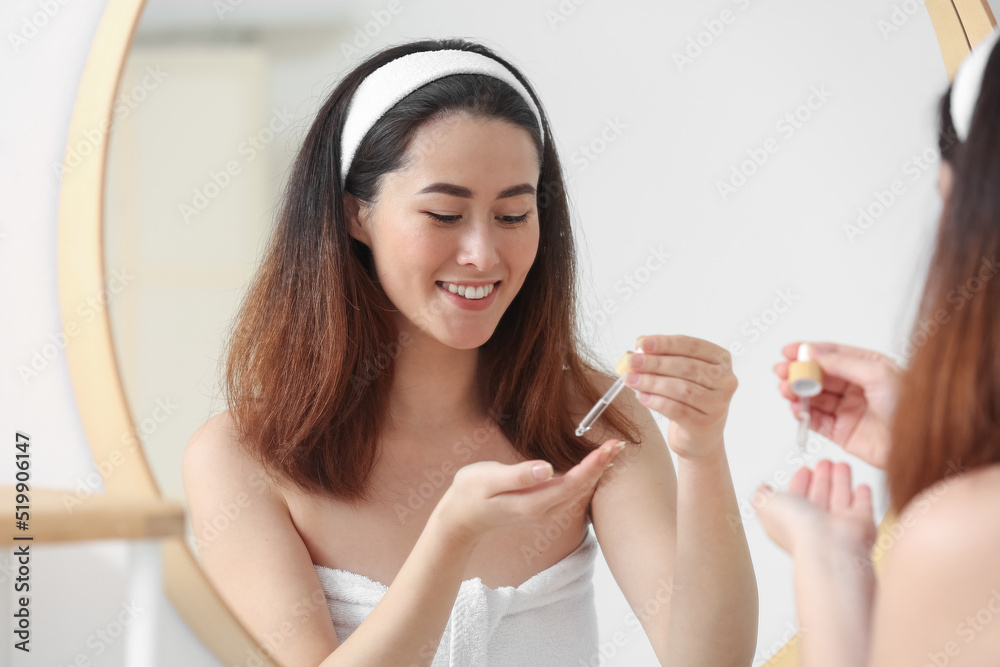 Young Asian woman using cosmetic serum in bathroom Young Asian woman using cosmetic serum in bathroom