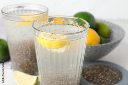 Glasses with water, chia seeds and sliced lemon on white table, closeup