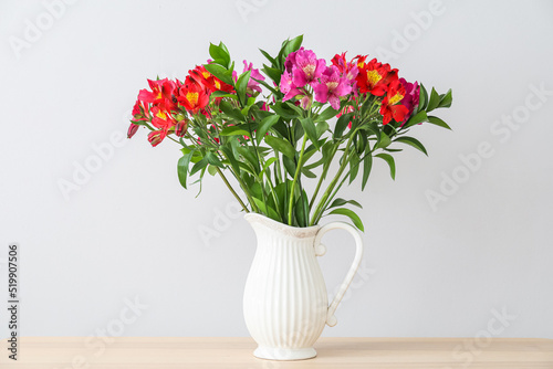 Vase with alstroemeria flowers on wooden tabletop against light wall