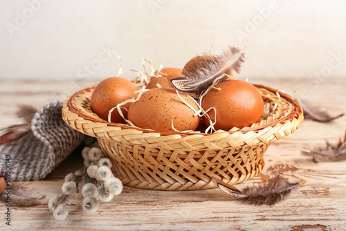 Wicker basket with eggs and pussy willow branches on light wooden table
