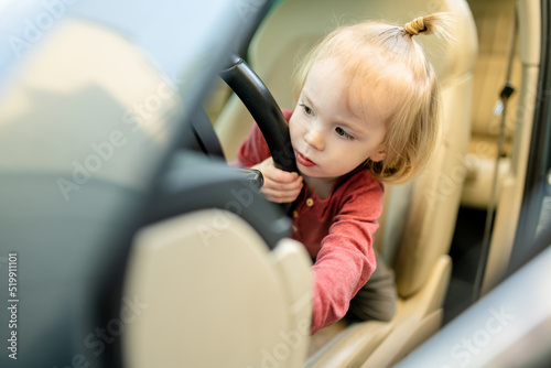 Adorable toddler boy playing in the driver's seat. Cute little son sitting in fathers car.