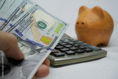hundred dollar cash bills, next to a clay piggy bank, with a calculator