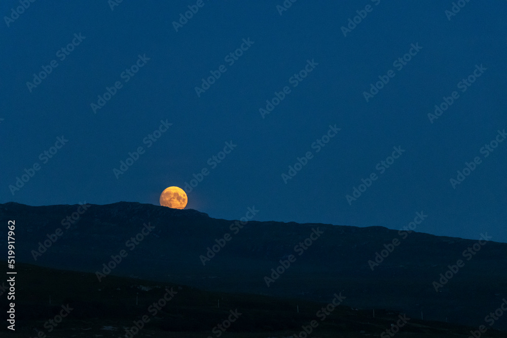 Bright orange full moon rising over silhouetted hills Bright orange full moon rising over silhouetted hills