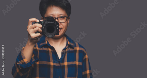 Portrait of a photographer in a blue shirt holding a digital camera while standing on a gray background