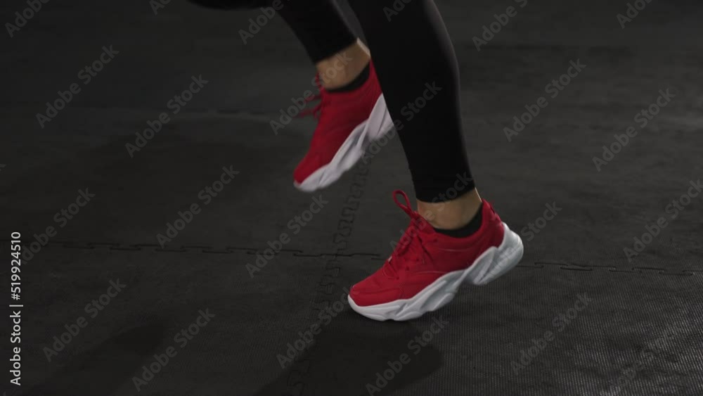 A young woman wearing red sports shoes running stationary to warm up before exercise in sports club, gym fitness training center, indoor workout.