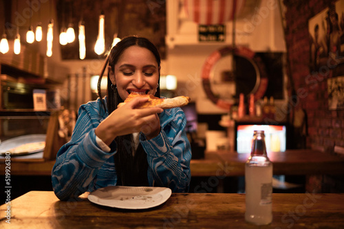 Pizza, food and restaurant where young woman is eating food and enjoying drinks. Hungry female having delicious meal at bar at night. Happy and satisfied foodie having tasty supper at a diner