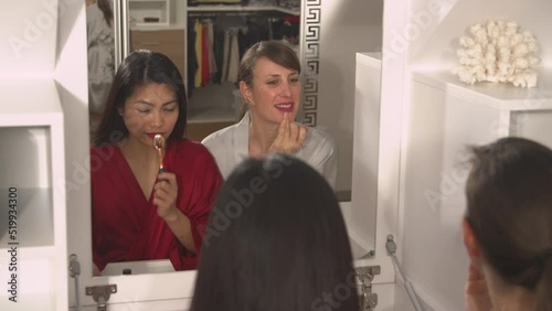 CLOSE UP: Mirror reflection of two attractive ladies applying their make up look. Two pretty women having a beauty treatment. Asian and Caucasian women using facial beauty products for a better look. photo