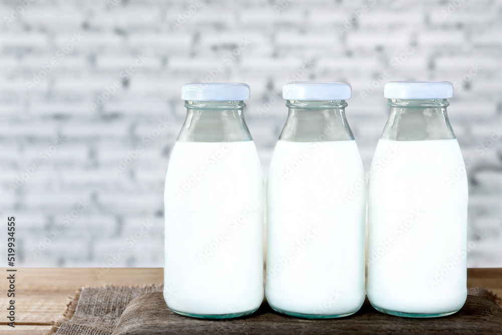 Three bottles of milk on a wooden table and white concrete wall background. Three bottles of milk on a wooden table and white concrete wall background.