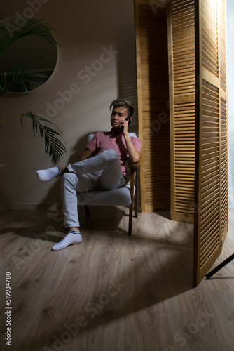 Businessman sitting in an armchair using smartphone at home calling photo