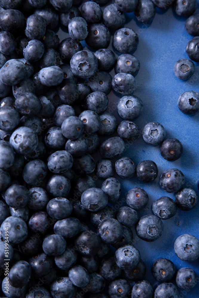 Vertical photo with scattered blueberries in a blue flat plate