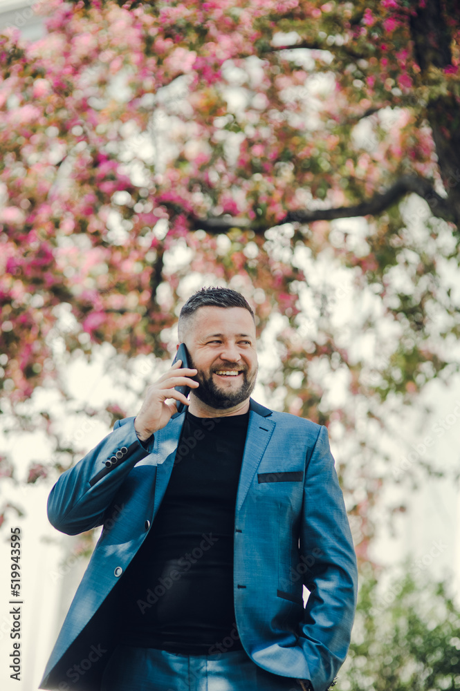 Handsome man businessman. European business people looking at wristwatch and talking on mobile with colleagues that late appointment in the park. Handsome man businessman. European business people looking at wristwatch and talking on mobile with colleagues that late appointment in the park.