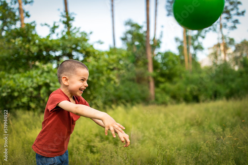 Portrait of little adorable boy playing ball in meadow in forest in summer