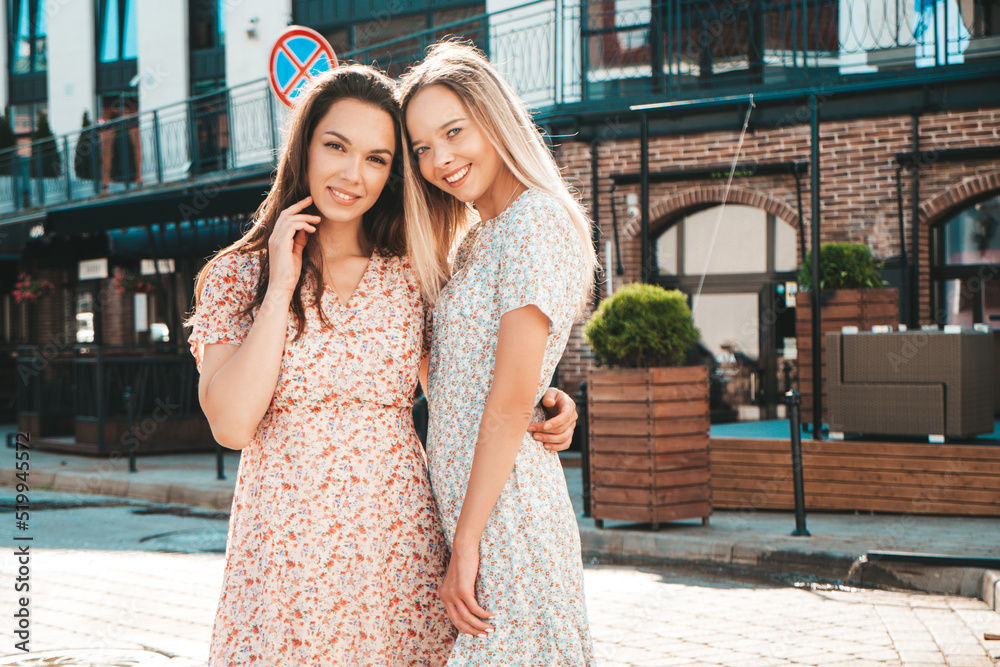 Naklejka premium Portrait of two young beautiful smiling hipster female in trendy summer dress clothes.Sexy carefree women walking on street background. Positive models having fun, hugging