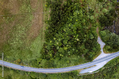 Aerial top down view on a small road and car park with white van by a green field and forest. Rural area and country side. West of Ireland. Transport industry and tourism.