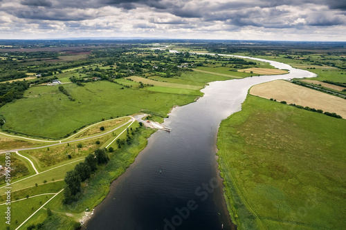River Shannon flows between green grass fields and agriculture land. Irish landscape. Low cloudy sky. Aerial view. Athlone, Ireland. photo
