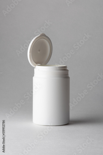 A white plastic pill container floating in the air on a gray background