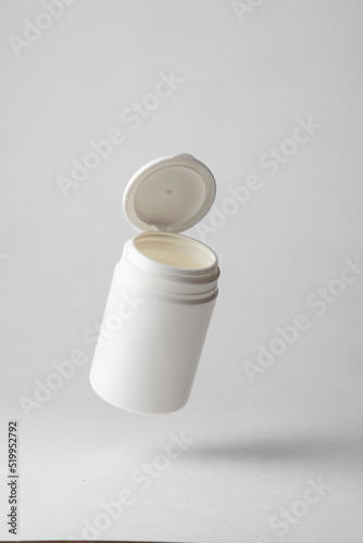 A white plastic pill container floating in the air on a gray background