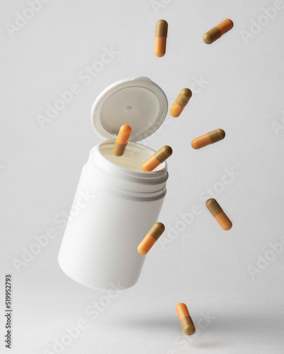 An orange-beige colored pill capsule falling out of a white plastic pill bottle on a light background.