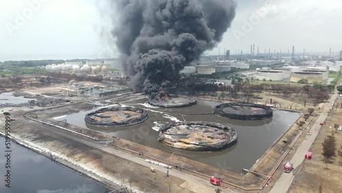 Aerial footage of a large scale Oil refinery with smoke because explosions stacks and petroleum storage tanks	
