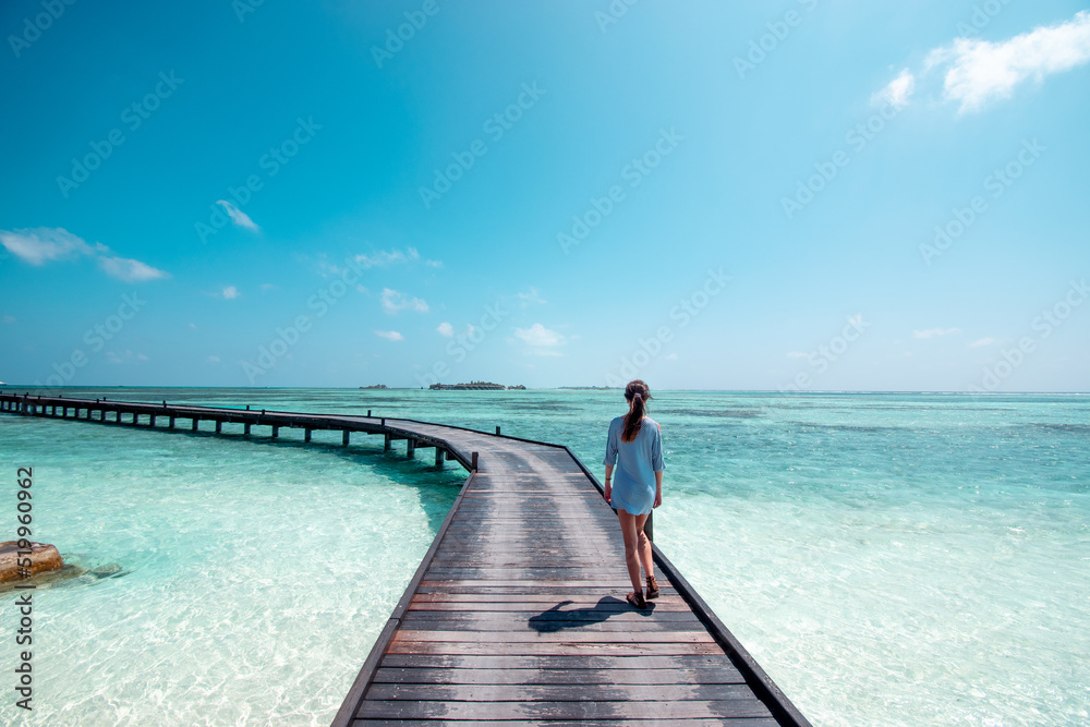 Woman on tropical island walking out into ocean on wooden pier in the Maldives