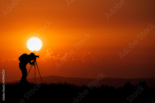 A professional photographer's silhouette is focused on shooting in a beautiful meadow.