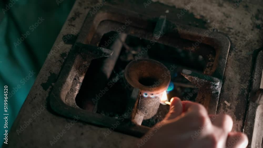 The hand brings a burning match to the burner of an old gas stove and