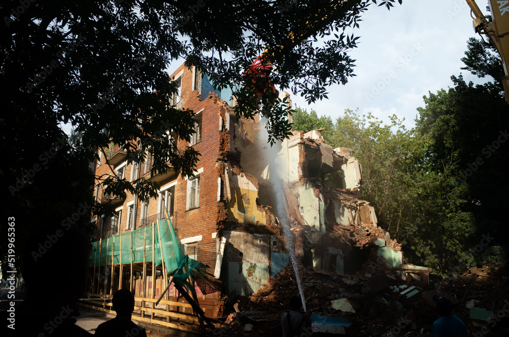 Fototapeta premium Demolition of a brick building with excavator mechanical arm. Destruction of dilapidated housing. Heavy machinery hydraulic construction equipment