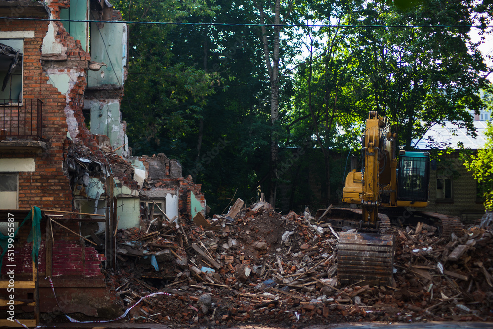 Demolition of a brick building with excavator mechanical arm. Destruction of dilapidated housing. Heavy machinery hydraulic construction equipment