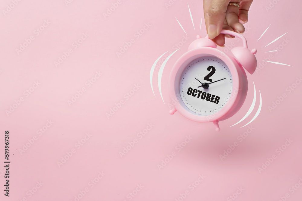 Obraz premium October 2nd. Day 2 of month, Calendar date. The morning alarm clock jumping up from the bell with calendar date on a pink background. Autumn month, day of the year concept.