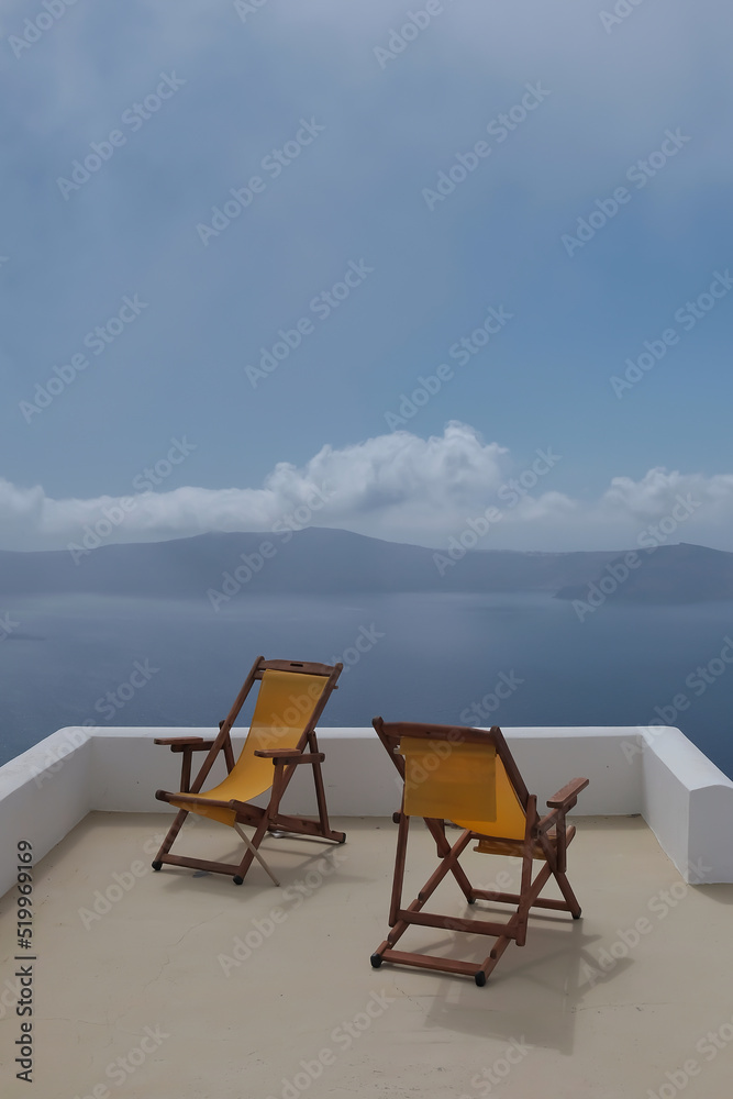 View of two empty sunbeds on the rooftop of a villa  and a spectacular view of the Aegean Sea  in Santorini Greece