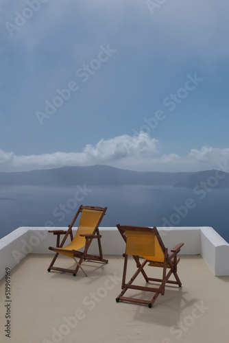 View of two empty sunbeds on the rooftop of a villa and a spectacular view of the Aegean Sea in Santorini Greece