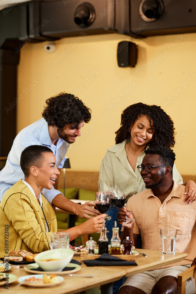 A group of multicultural friends toasts with red wine at the winery.