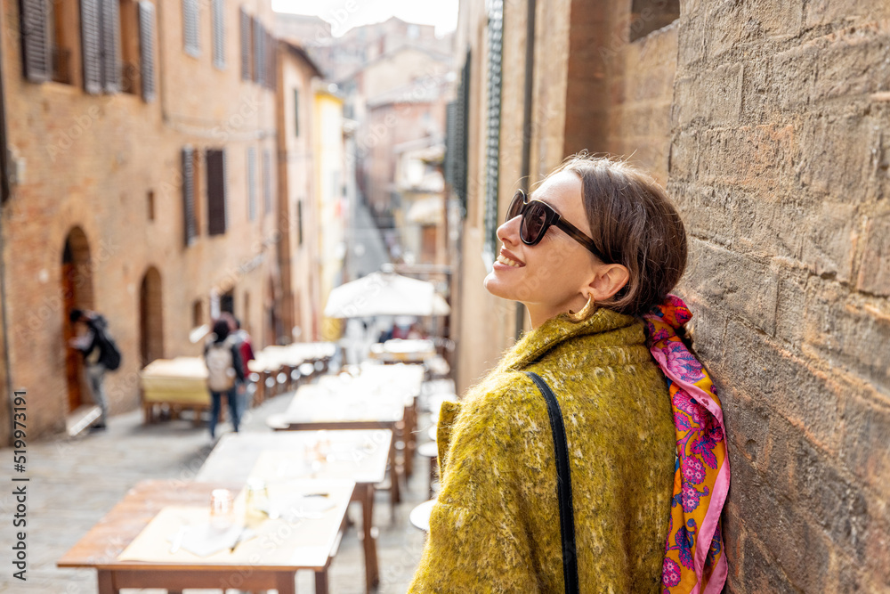 Obraz premium Sylish woman walks on narrow and cozy street in old town of Siena city. Concept of traveling in Tuscany region and italian lifestyle