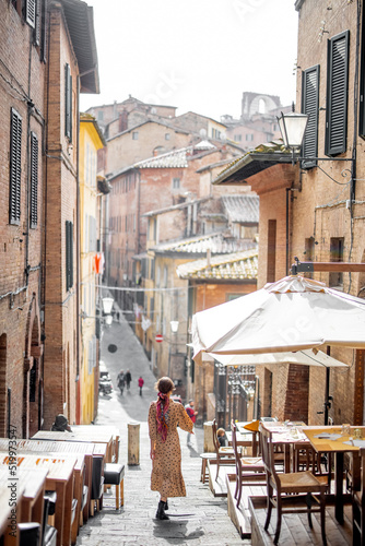 Sylish woman walks on narrow and cozy street in old town of Siena city. Concept of traveling in Tuscany region and italian lifestyle
