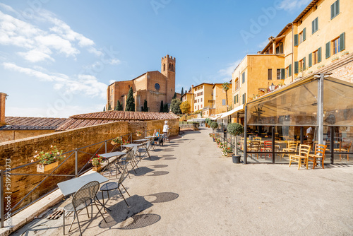 Fototapeta Naklejka Na Ścianę i Meble -  View on the street with restaurant tables and San Domenico basilica in Siena town. Traveling landmarks in Tuscany region of Italy